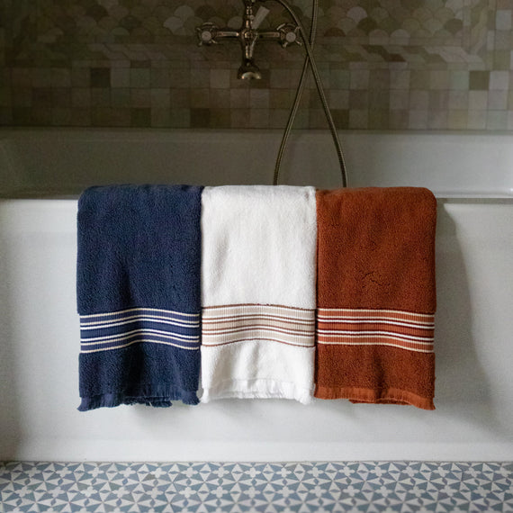 Our Madison Towels in denim, white, and rust colorways folded over a white bathtub.